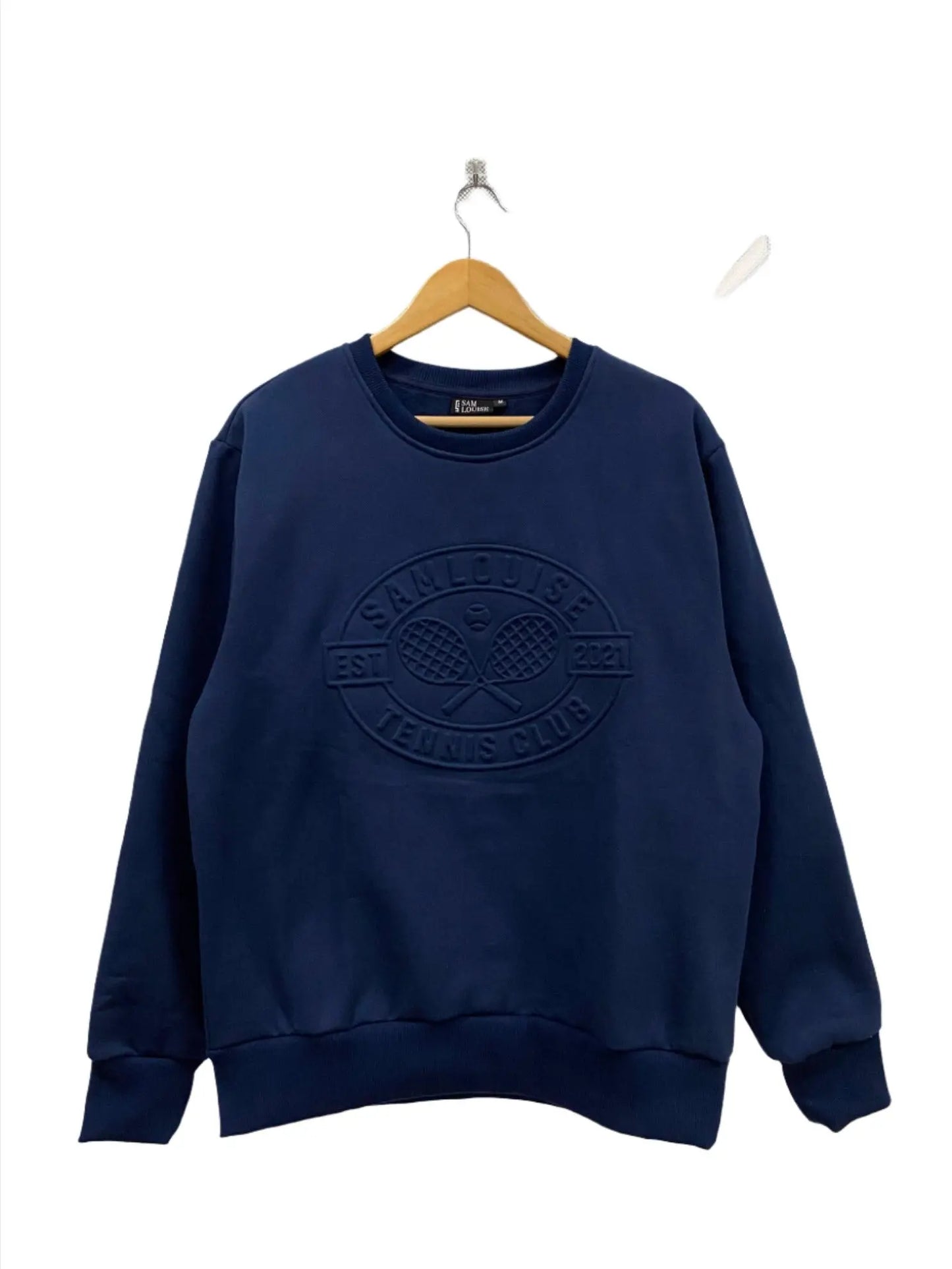 Close-up of the SamLouise Tennis Club Embossed Sweatshirt in cream, featuring raised lettering and imagery. The design includes 3D crossed tennis rackets and a tennis ball, encircled by the text TENNIS CLUB and 2021.