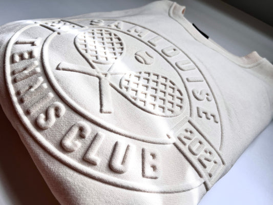 Close-up of the SamLouise Tennis Club Embossed Sweatshirt in cream, featuring raised lettering and imagery. The design includes 3D crossed tennis rackets and a tennis ball, encircled by the text TENNIS CLUB and 2021.