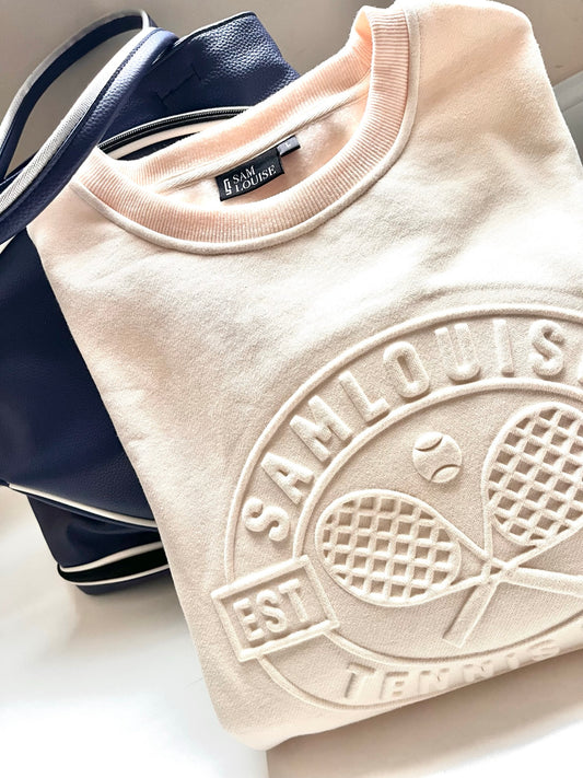 Close-up of the SamLouise Tennis Club Embossed Sweatshirt in cream, featuring raised lettering and imagery. The design includes 3D crossed tennis rackets and a tennis ball, encircled by the text TENNIS CLUB and 2021.